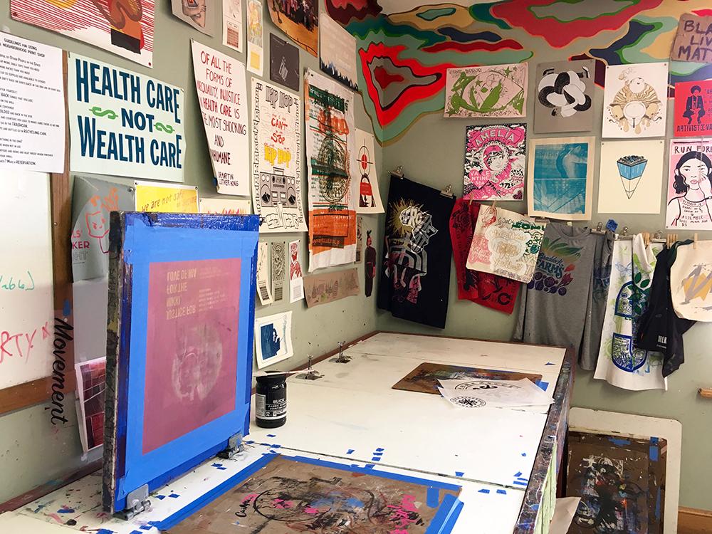 The print shop walls are covered by prints in many colors. A screen print sits open on the table. Photo by Arielle Berk.