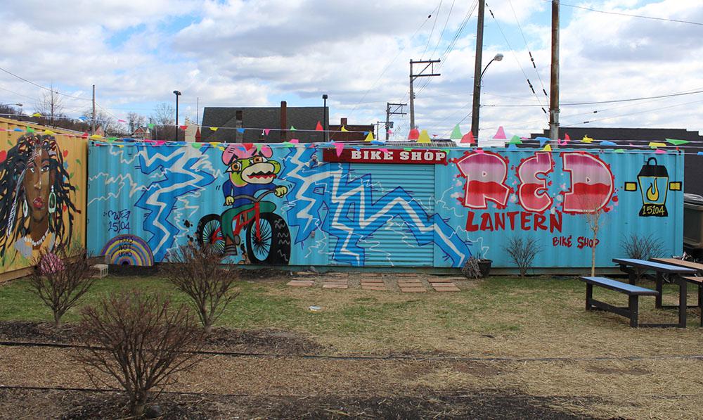 The front of the Red Lantern Bike Store and the side of the Free Store's secondary shipping container, both displaying creative paintings.