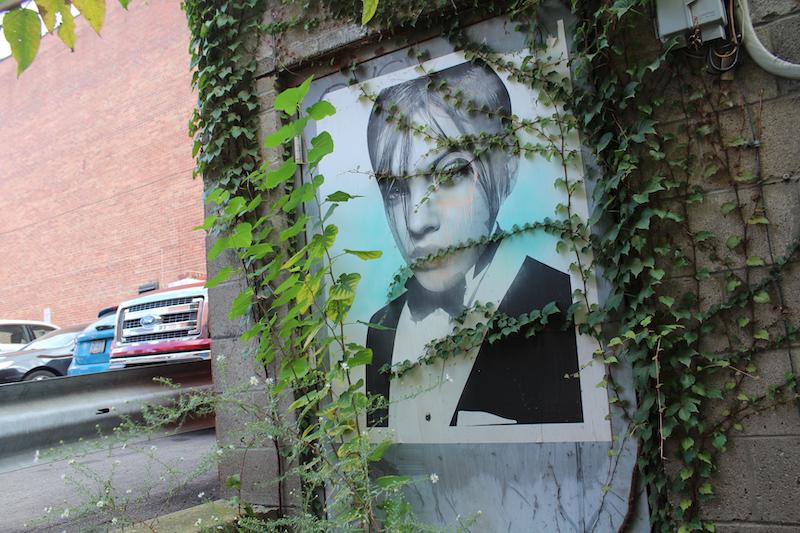 A small painting of a boy in a suit covered in green vines. The was found in the alley besides Primanti Bros. Photo by Kyra Moore, 2019