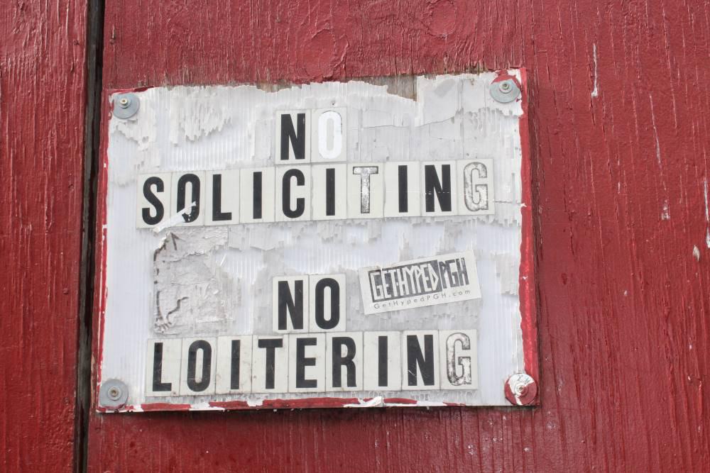 "No Soliciting. No Loitering" sign on red fence along Penn Ave. Photo by Kyra Moore, 2019